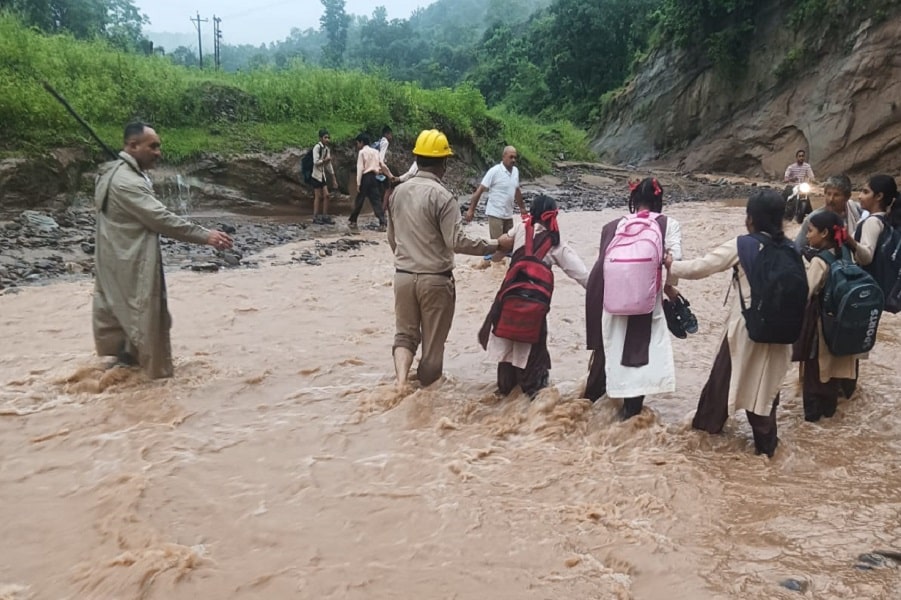 मातर में उफनती नदी और पहाड़ी खाले के बीच फंसे स्कूली बच्चों और स्टाफ सदस्यों को होमगार्ड के जवान सुरक्षित निकालते हुए